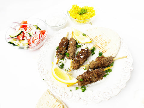 kafta de ternera en un plato blanco con ensalada griega cocinada en una sartén salteada a rayas con tapa de cristal