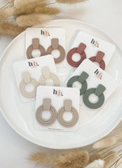 Image shows platter containing 5 pairs of circular pendant earrings in red, green, beige, cream, brown