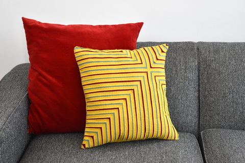 Textured throw pillows in red and yellow resting on a gray couch.