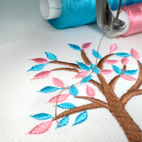 Machine embroidery sample tree with pink and blue leaves on white fabric