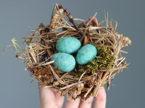 Wet felted wool robin eggs inside a handmade nest of twigs and moss.