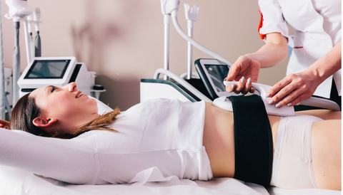 Esthetician straps ems paddle to the female customer abdominal area 