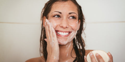 Happy woman with wet hair washing her face, holding bar of soap 