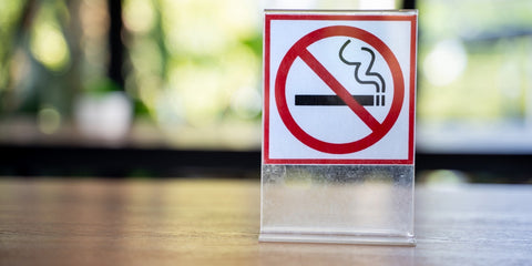 No Smoking sign on a shiny wooden surface, greenery in background 