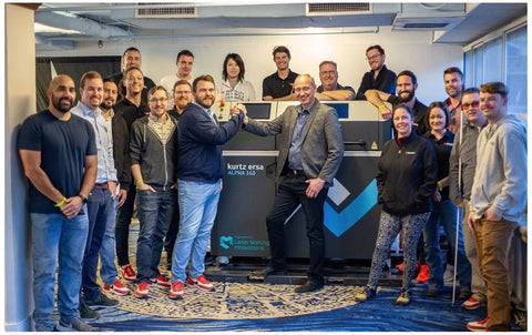 The Kurtz Ersa and Würth Additive Group are standing around an Alpha 140 industrial 3D printer, celebrating their recent partnership. 