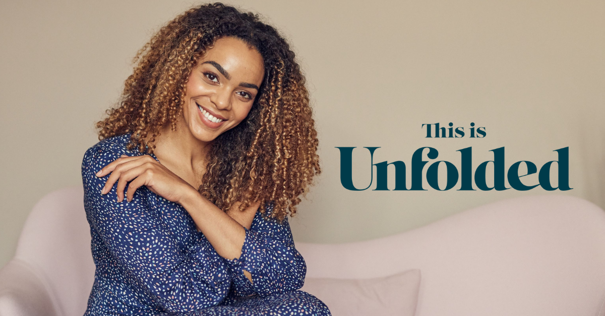 A woman with curly hair in a blue blouse on a pink sofa, next to a This is Unfolded logo