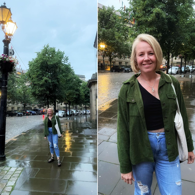 Person standing on a wet, cobblestone street near trees and buildings, smiling at the camera.