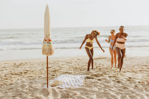 group of girls at the beach with an umbrella and blanket