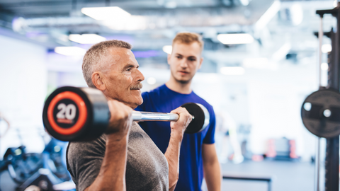 Senior man over 50 doing a bicep curl at gym with a personal trainer