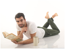 man reading book and lying on ground wearing white almo t-shirt and rifle green trackpants