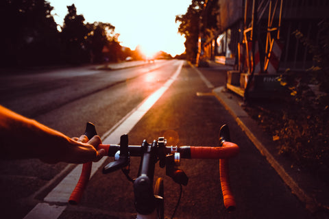 shot at dusk of a man on a bike with handlebars in foreground and an empty road in front of him