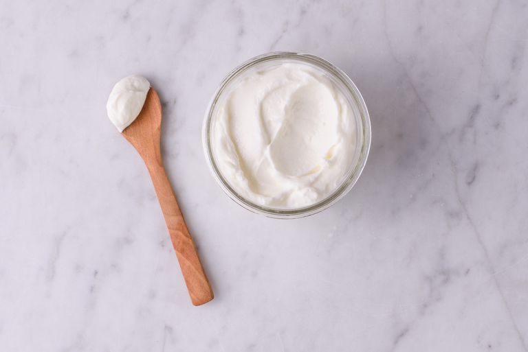 A glass bowl of plain yogurt with a wooden spoon