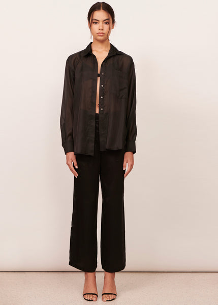 Woman wearing a semi sheer black silk oversized shirt and long black silk pants