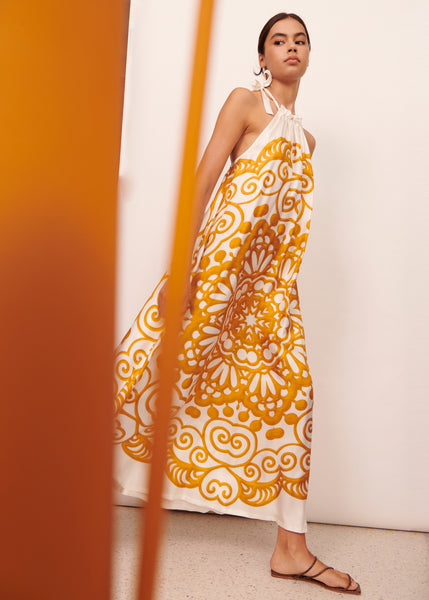 Woman walking wearing a white and orange silk halter maxi dress