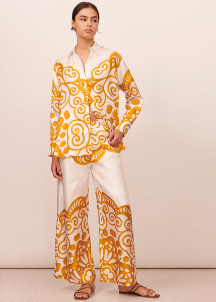 Young woman wearing an oversized white silk shirt with orange lace print and matching pants