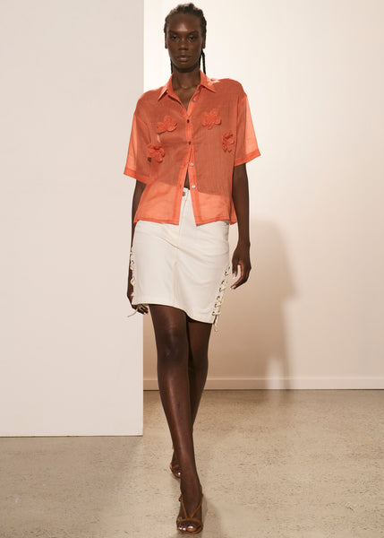 Akelo wears the Abi Flower Shirt in Brick with the Madi Denim Tie Skirt in White.