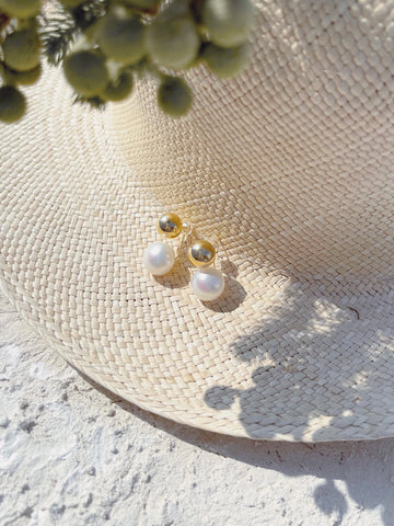 A straw hat adorned with pearls and a white flower, complemented by a pearl piercing.