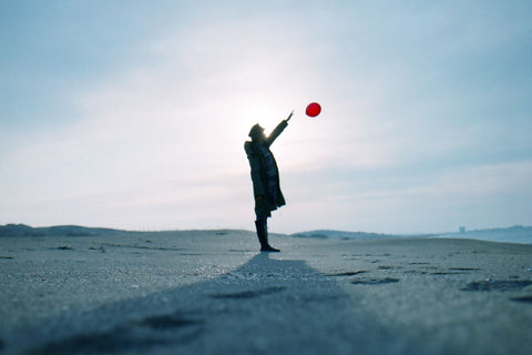 Male standing on sandy beack letting go of red balloon