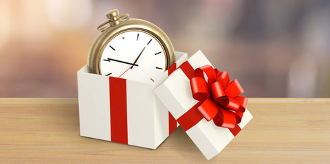 A gold pocket watch displayed within a white gift box with a red bow on a wooden table