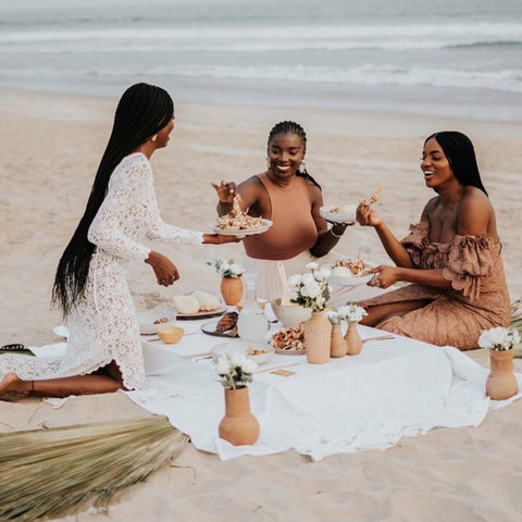 Group of 3 black women having a picnic on a white sandy beach lainging and smiling