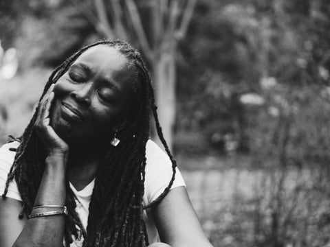 Black female with her head resting in her hands displying a content facial expression in the park