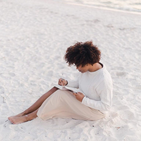 Lady writing in her journal sitting down on a white sandy beach