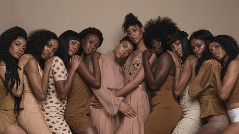 A group of black females with different skin tones stanting and resting their head on one another