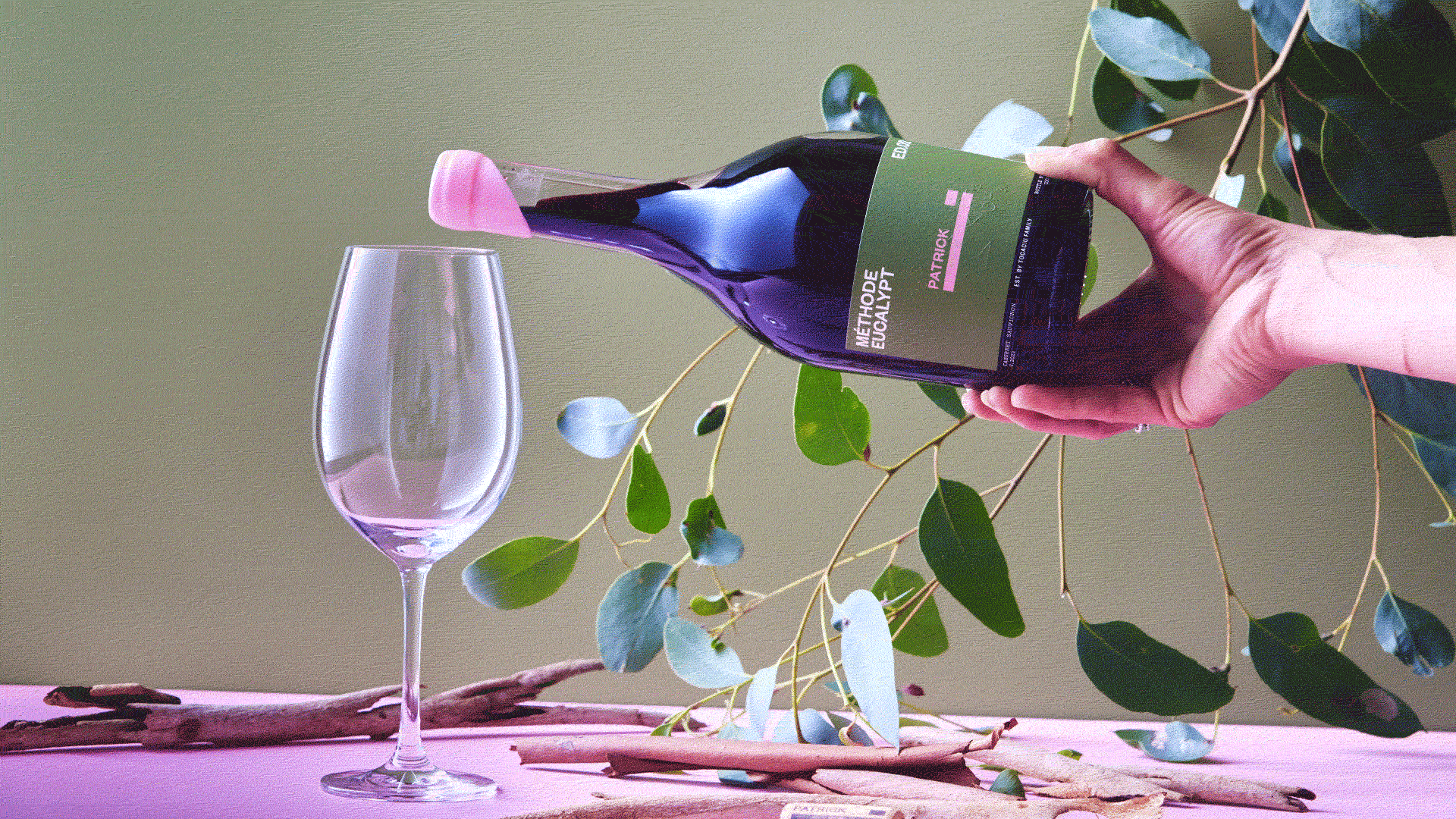 Gif of someone pouring a bottle of red wine into a glass against an olive background.