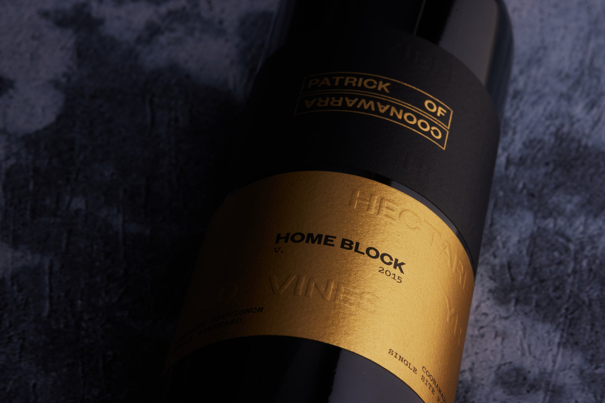 Bottle of red wine zoomed in on the gold embossed label against a dark background.
