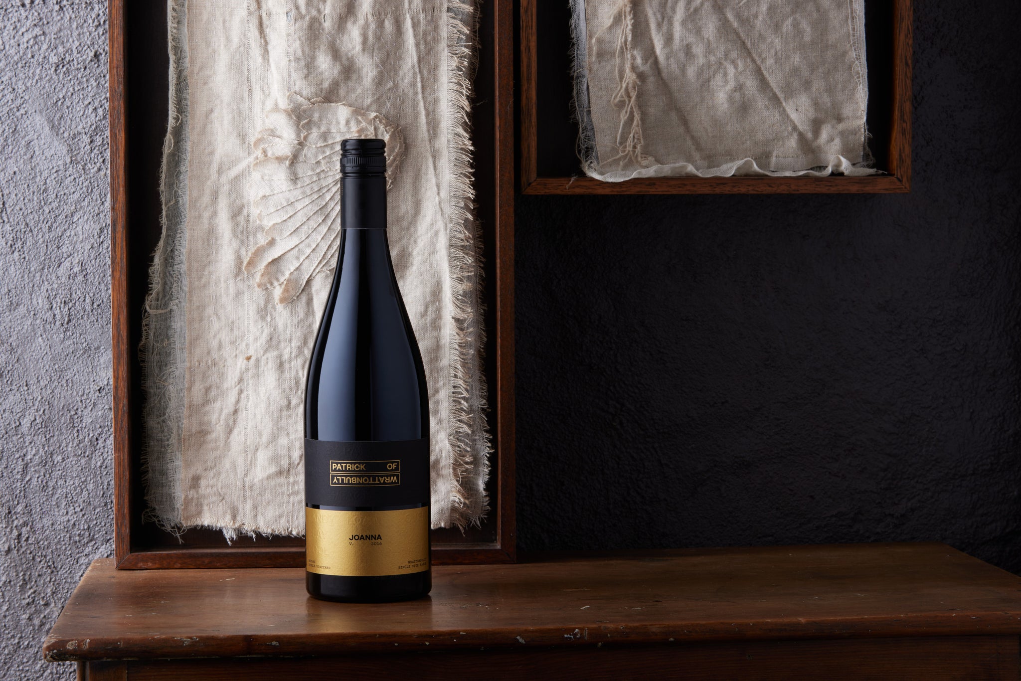 Bottle of wine with a black and gold label in front of a linen and wood background.