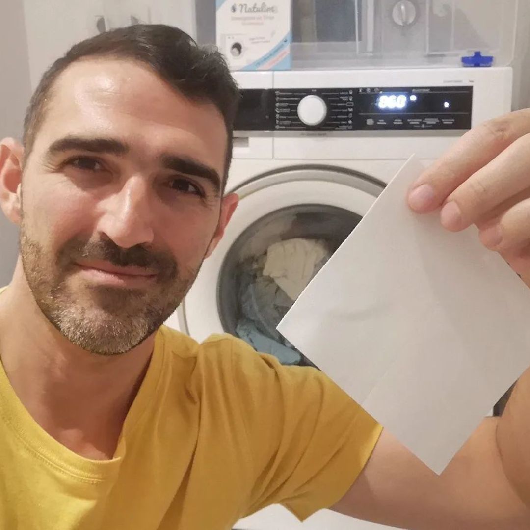 Man holding a sheet in front of a washing machine.