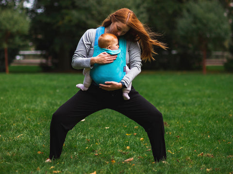 Llevar a un bebé en cabestrillo durante la práctica de yoga en el parque, pose de diosa