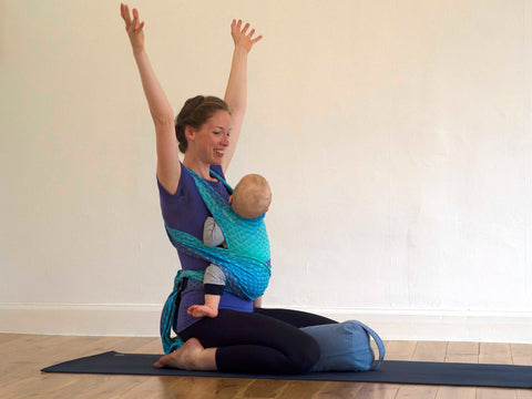 Bebé en un cabestrillo durante la práctica de yoga, postura virasana