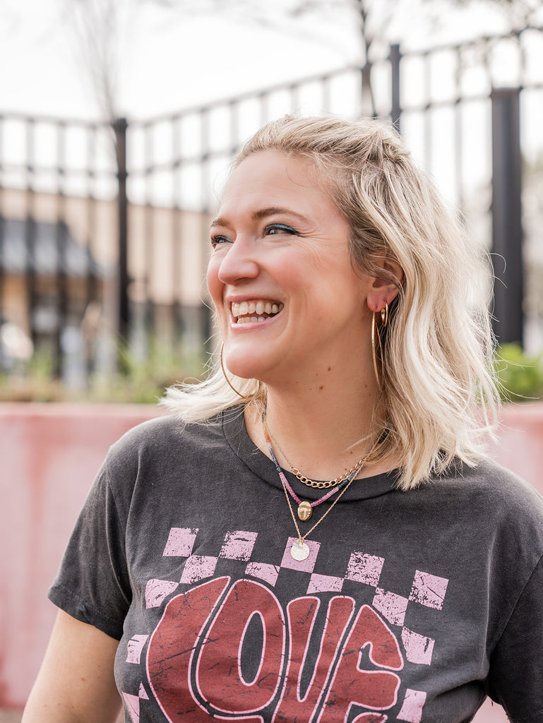 Kenda Kistenmacher is laughing while wearing a graphic tee and layered gold jewelry