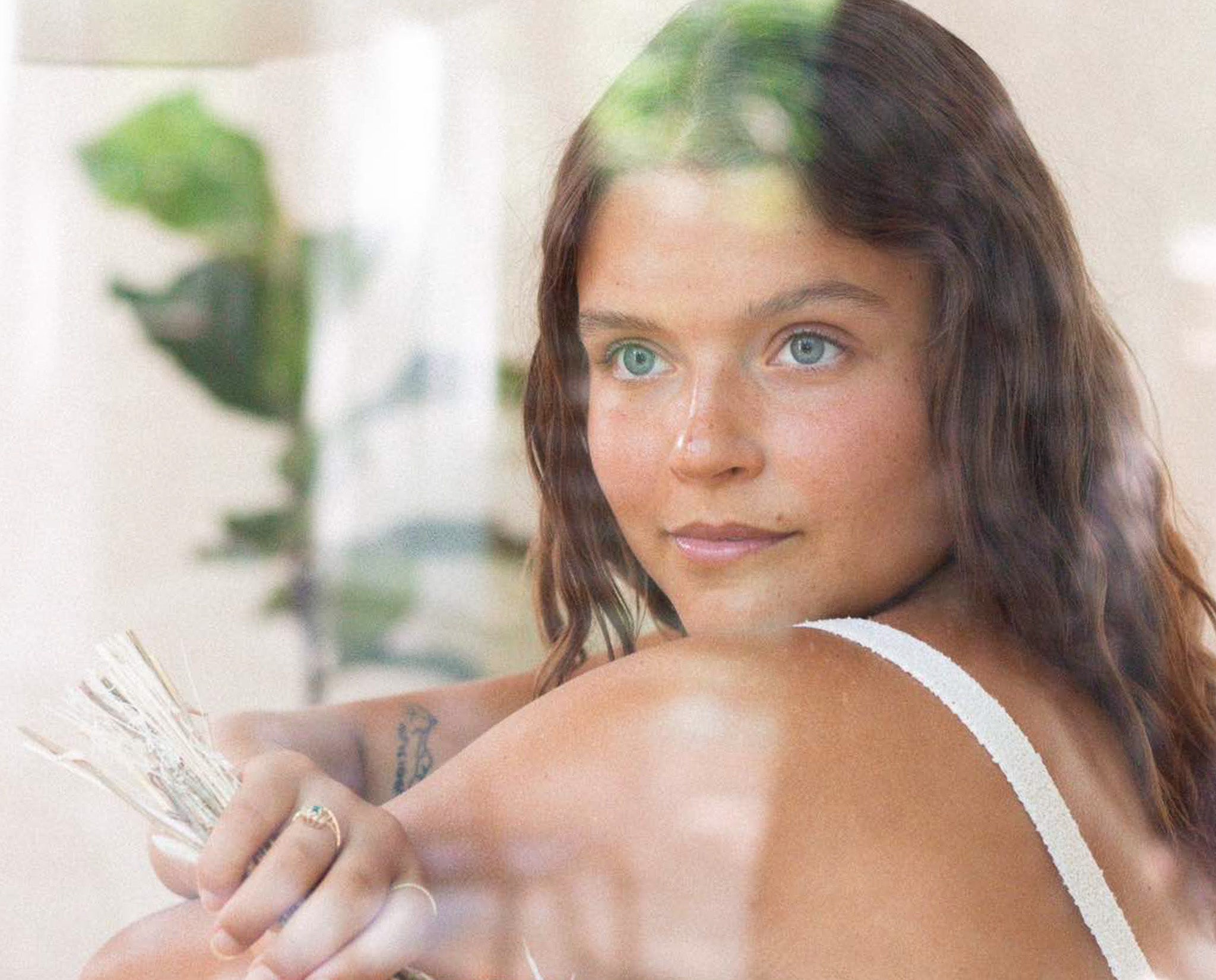 Woman with a tattoo holding a bundle of money, looking at the camera through a glass window.