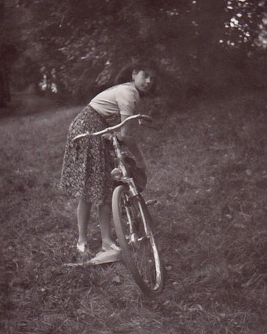 a black and white photo of a young woman in the 1940's leaning over her bicycle.