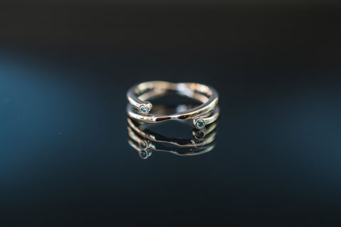 a silver double banded ring with lab grown blue diamonds sits atop a black mirrored surface