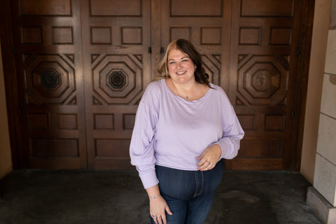 Founder Ashley stands in front of a doorway in Balboa Park wearing a lavender sweatshirt, jeans and Chouette Designs silver and tanzanite jewelry.