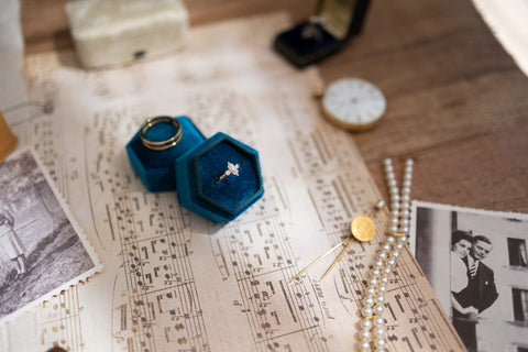A flat lay featuring an engagement ring in a blue velvet box atop sheet music