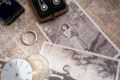 a flat lay of a silver ring, pocket watch, vintage earrings and a silver franc on top of french script and old photographs