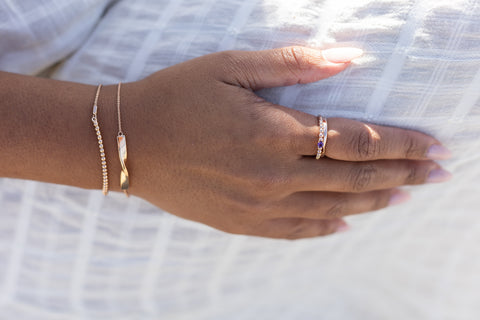 a hand rests on a white linen dress with rose gold bracelets and rose gold rings on.