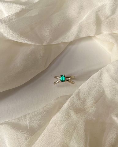 a criss cross style Emerald ring is framed by ethereal fabric