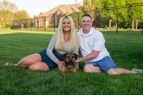 Foster dog mom and dad sitting in grass with brown foster dog