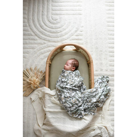 Baby wrapped in swaddle in a bassinet on a rug looking to the side