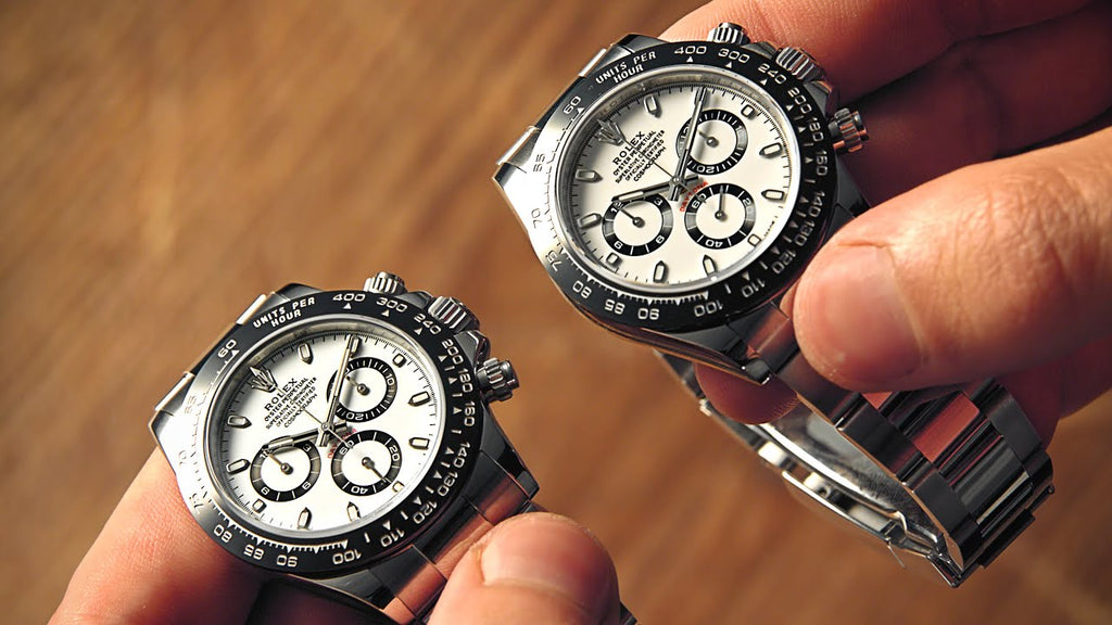 Someone holding two stainless steel Rolex Daytona next to eachother, one of them being fake and the other is real