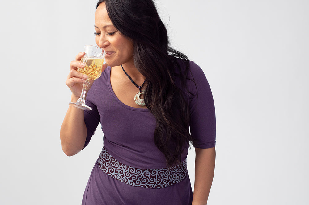 Woman wearing purple dress and purple patterned belt, drinking from a glass