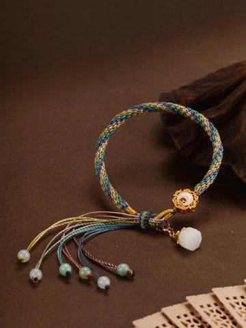 Close-up of hands threading beads on a string, with a variety of jewelry stringing materials laid out on the table