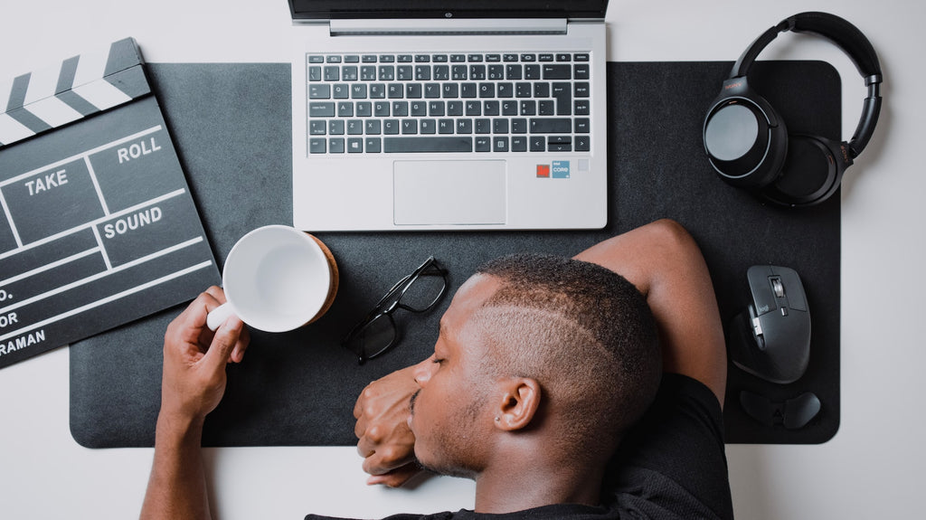 A man is sleeping on his laptop and holds a cup of coffee in his left hand