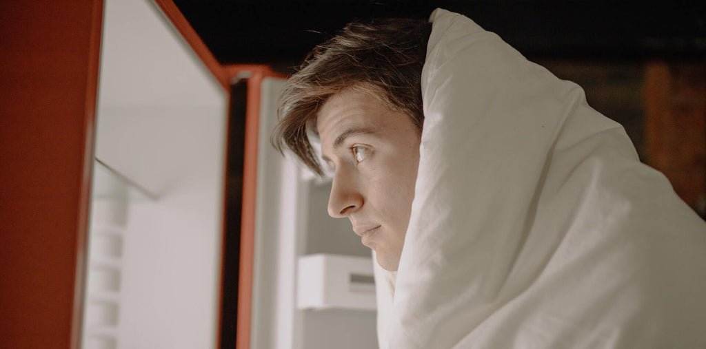 A man looking in the fridge covered in the blanket