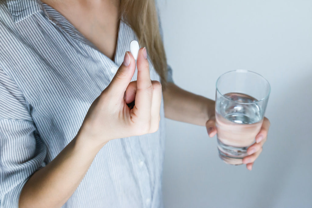 A woman with the glass of water and a pill aware of dehydration